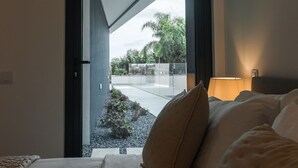 A modern hotel room with a bed, a nightstand, and a view of a landscaped area outside. - Buganvilia - Luxury villa - private pool by HD (Almancil)