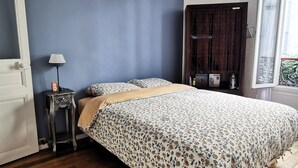 A bedroom with a bed, a nightstand, a lamp, a wardrobe, and a window. - Bienvenue à Paris 19 :) (Paris)