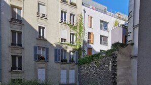 A courtyard with potted plants, a stone wall, and a balcony railing. - Bienvenue à Paris 19 :) (Paris)