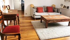 A living room with a wooden coffee table, grey sofa with red cushions, and a dining table with chairs. - Bienvenue à Paris 19 :) (Paris)