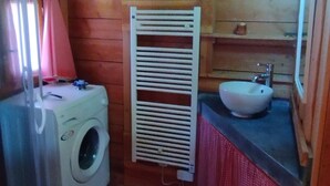 Pieni kylpyhuone, jonka seinät ovat puuta, ja jossa on pyykinpesukone, pesuallas ja pyyhekoukku.