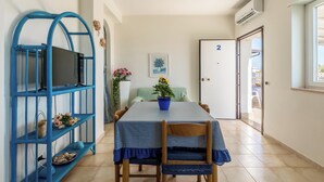 A dining area with a table, chairs, a blue metal shelf, a potted plant, and a door marked with the number 2. - 3866 Horizont - Bilo Standard by Barbarhouse (Margherita di Savoia)