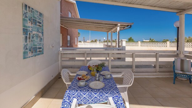 A covered outdoor dining area with a table set for two, a blue and white tablecloth, and a view of the sea in the background. - 3866 Horizont - Bilo Standard by Barbarhouse (Margherita di Savoia)