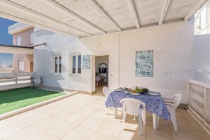 A covered patio with a dining table set for two, a green artificial lawn, and a view of the sea. - 3866 Horizont - Bilo Standard by Barbarhouse (Margherita di Savoia)