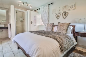 Un dormitorio con una cama grande, una mesita de noche, una lámpara, un espejo y una zona de ducha.