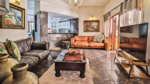 Ein großzügiges Wohnzimmer mit Ledersofas, einem Couchtisch und einem Fernseher. An den Wänden befinden sich Dekorationen und Kunstwerke.