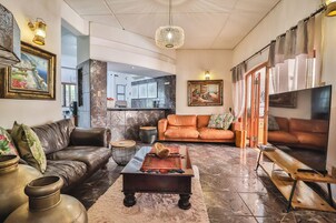 Amplia sala de estar con sofás de cuero, una mesa de centro y un televisor. Se observan elementos decorativos y obras de arte en las paredes.