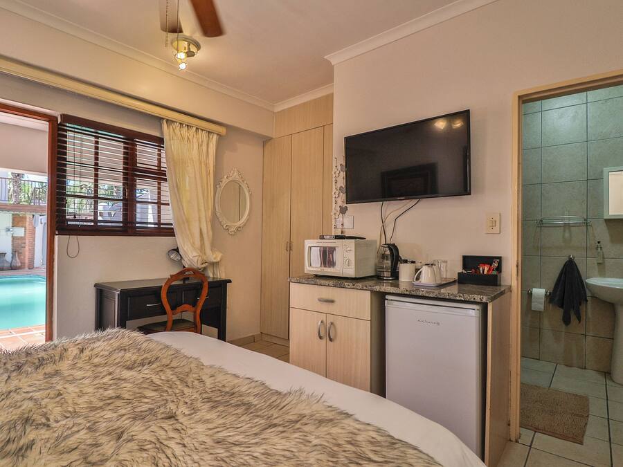 A bedroom with a bed, a desk, a television, a microwave, a sink, and a view of a swimming pool.