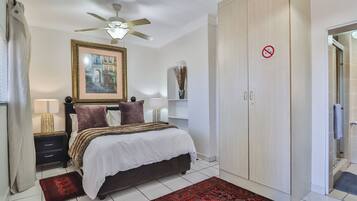 A bedroom with a bed, nightstands, a ceiling fan, a wardrobe, and a bathroom door.