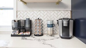 En köksbänk med en kaffebryggare, ett ställ för kaffemuggar och en hylla med små växter och en skylt med texten ”hem”.