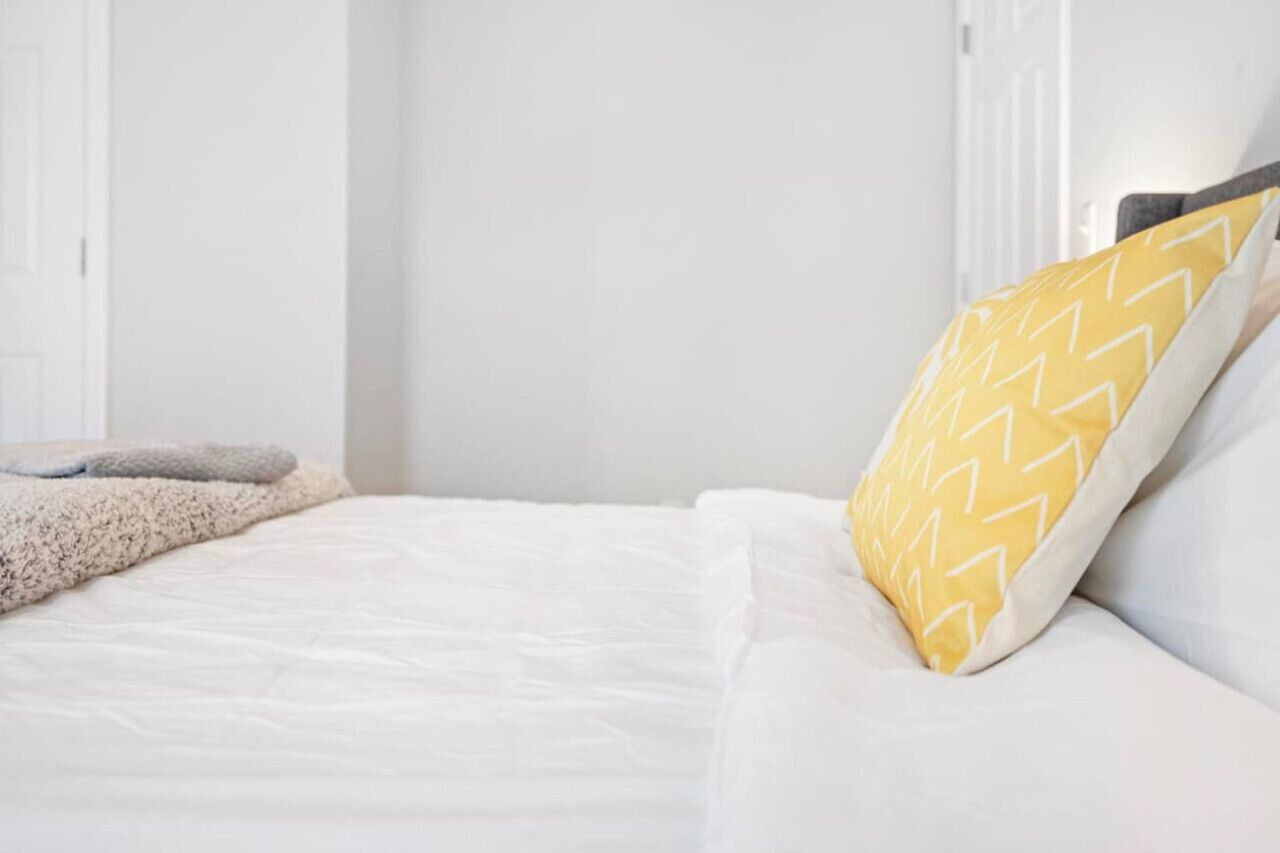 A neatly made bed with white bedding and a single yellow pillow with a zigzag pattern.