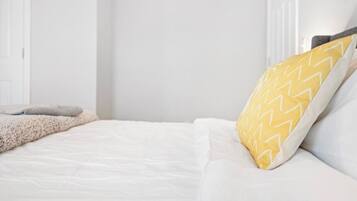 A neatly made bed with white bedding and a single yellow pillow with a zigzag pattern.