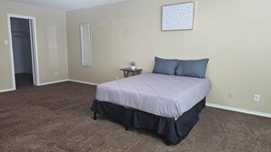 Une chambre à coucher avec un lit, une petite table sur laquelle est posée une plante, un miroir et un interrupteur fixé au mur.