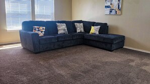 Un canapé modulable avec trois coussins, un tableau abstrait encadré et un sol recouvert d’une moquette.