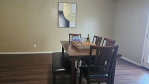 Une salle à manger avec une table et des chaises en bois, un panier rempli de fleurs et un tableau accroché au mur.