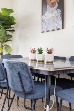 Un coin repas avec une table en marbre, des chaises en velours bleu et trois plantes en pot.