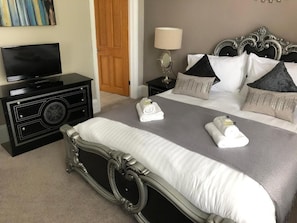 A neatly arranged bedroom with a large bed, a television on a dresser, and a bedside table with a lamp. - Washington house hotel (Bournemouth)