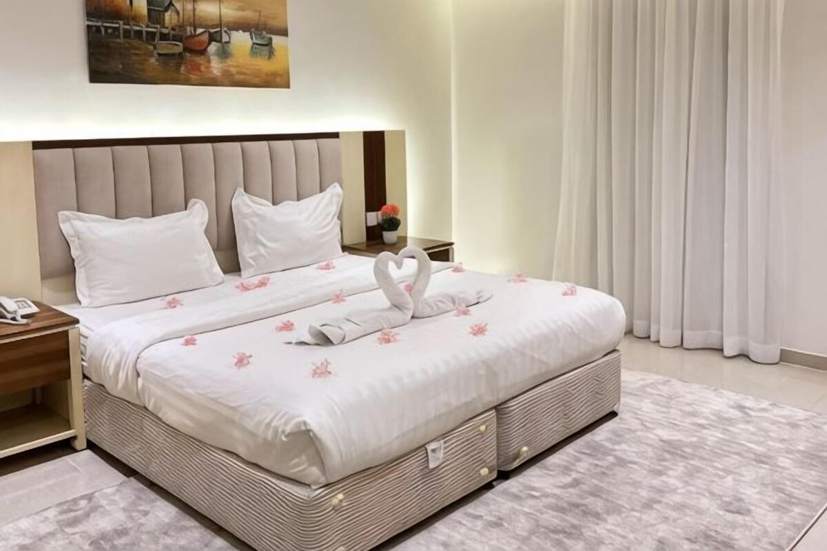 Una cama bien hecha con colcha blanca, dos almohadas y una decoración de toallas con forma de corazón.