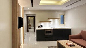 A modern hotel room with a flat-screen TV mounted on the wall, a kitchenette with a microwave, a coffee maker, and a small dining table. - Tamaya Alkhobar (Al Khobar)