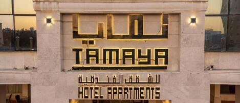 Entrada de un hotel con el nombre "Tamaya" y "Hotel Apartments" en árabe e inglés.