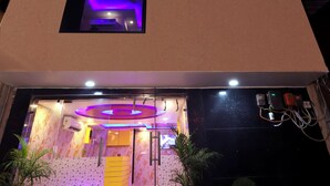 A hotel with a modern design, featuring a flat roof and large windows. The entrance has a glass door and is illuminated by interior lighting. There are potted plants at the entrance. - Jupiter Plaza (New Delhi)