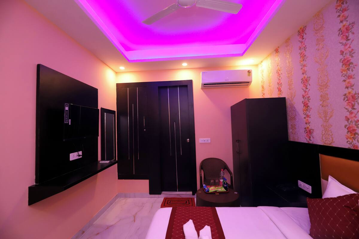 A hotel room with a bed, a TV mounted on the wall, a ceiling fan, and a small table with a chair.