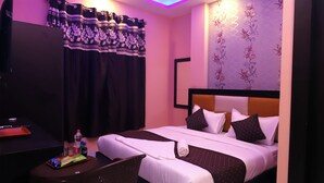 A hotel room with a bed, a desk, a chair, a ceiling fan, and a TV. - Jupiter Plaza (New Delhi)