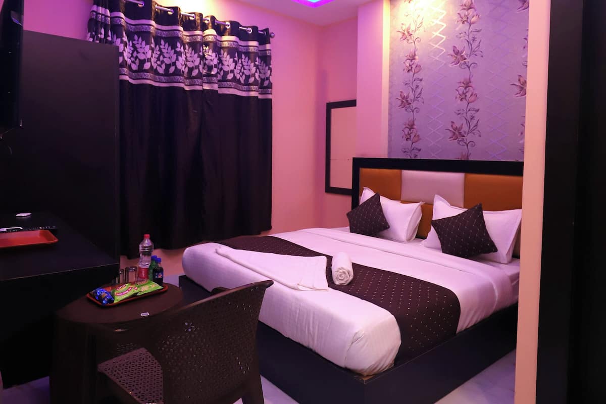 A hotel room with a bed, a desk, a chair, a ceiling fan, and a TV.