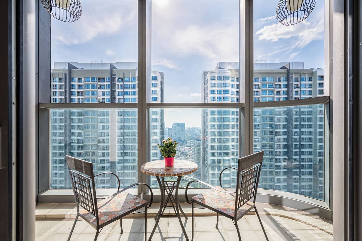 A balcony with a round table and two chairs, a potted plant, and a view of high-rise buildings.