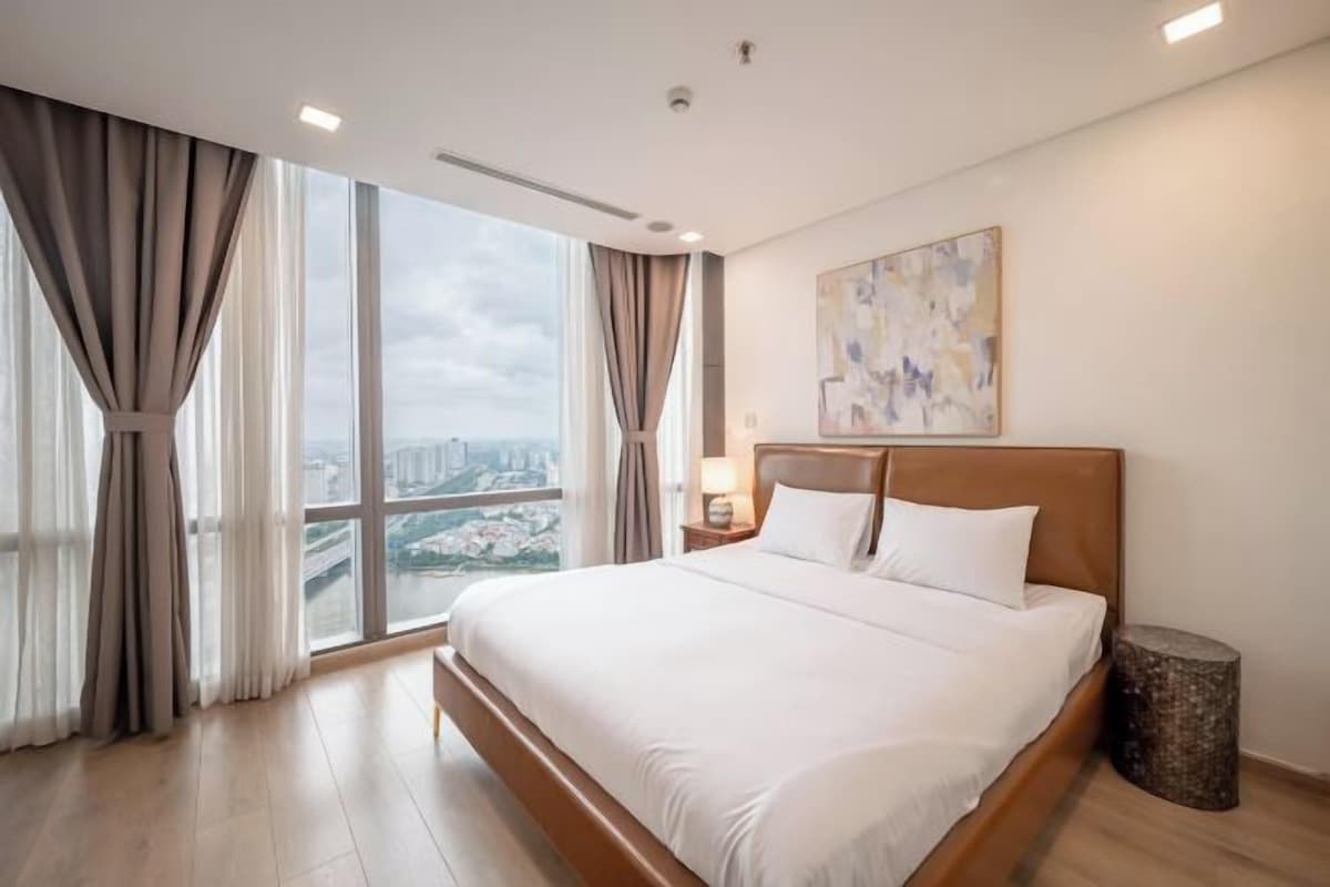 A hotel room with a large bed, a view of the city, and a painting on the wall.