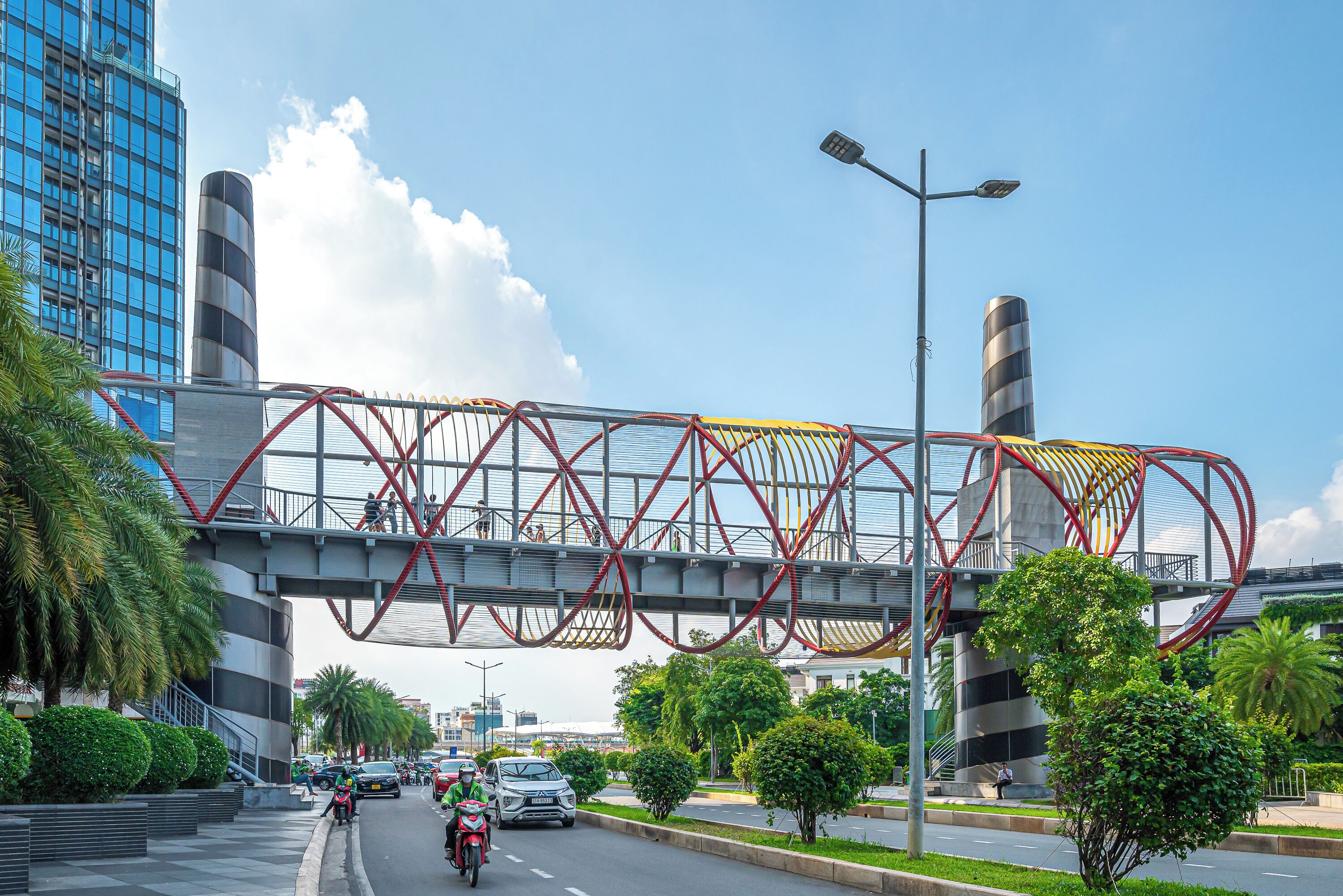 A modern urban street with a pedestrian bridge, cars, and greenery.