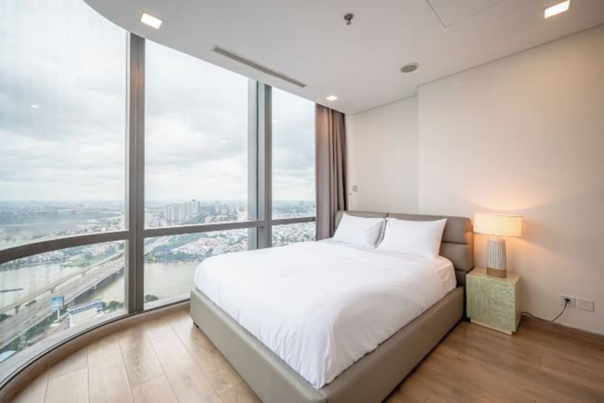 A bedroom with a large window, a bed, a nightstand, and a lamp.