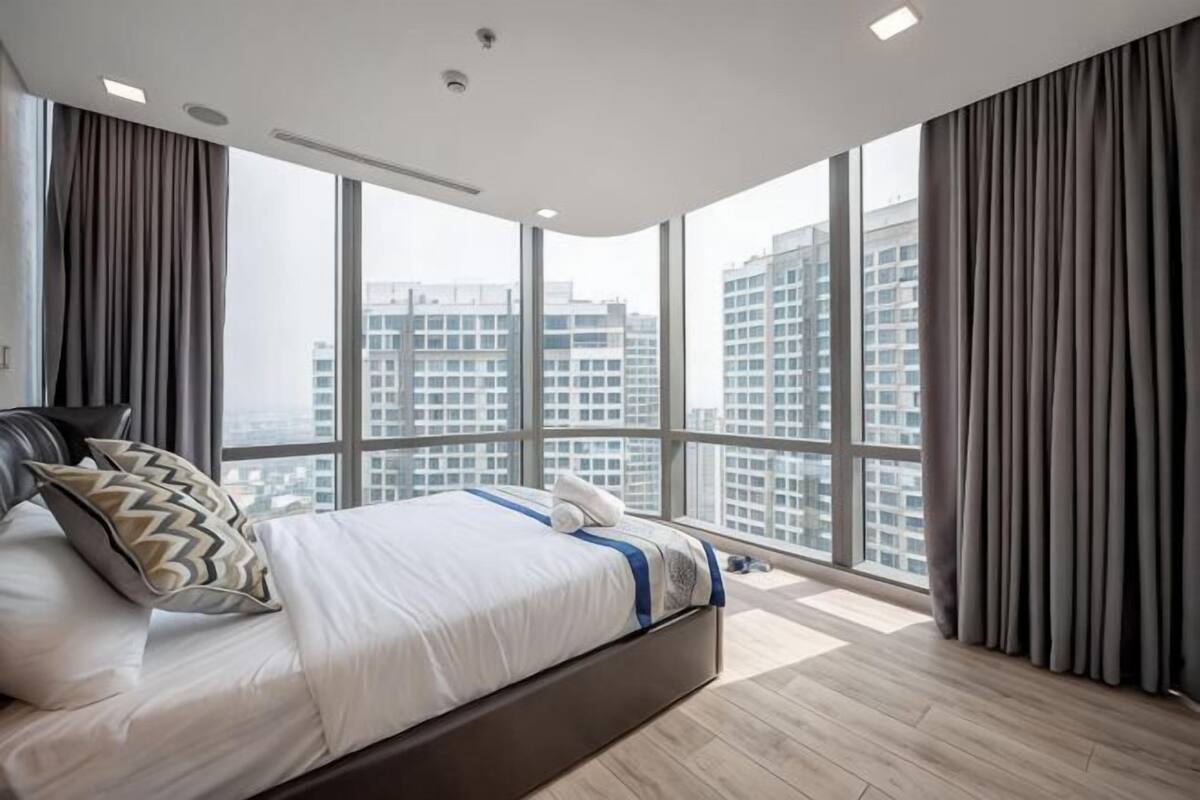 A modern bedroom with a large bed, a view of high-rise buildings, and a balcony.