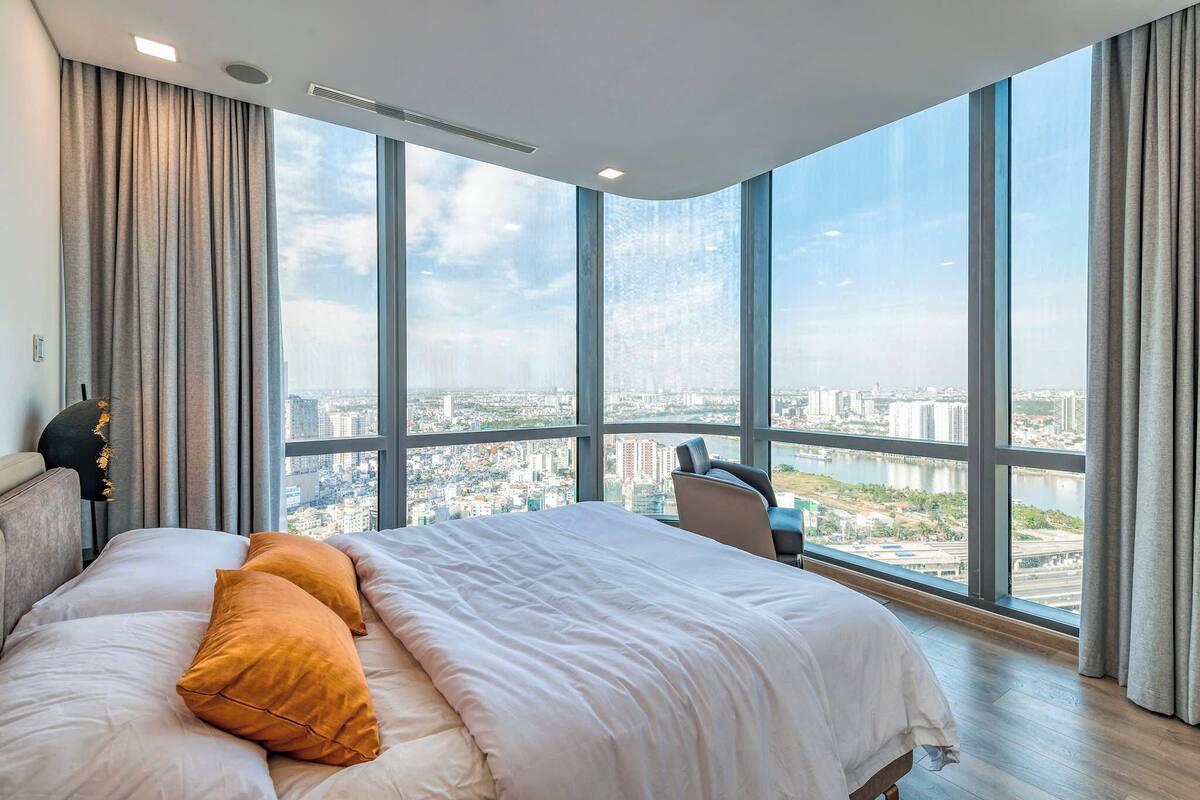 A modern hotel room with a large bed, a view of a cityscape through floor-to-ceiling windows, and a city skyline visible through the window.