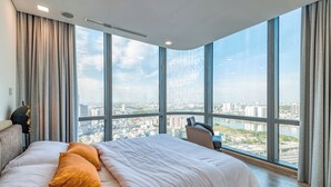 Une chambre d’hôtel moderne dotée d’un grand lit, offrant une vue sur le paysage urbain grâce à de grandes fenêtres du sol au plafond, et permettant d’admirer la silhouette de la ville à travers la fenêtre.