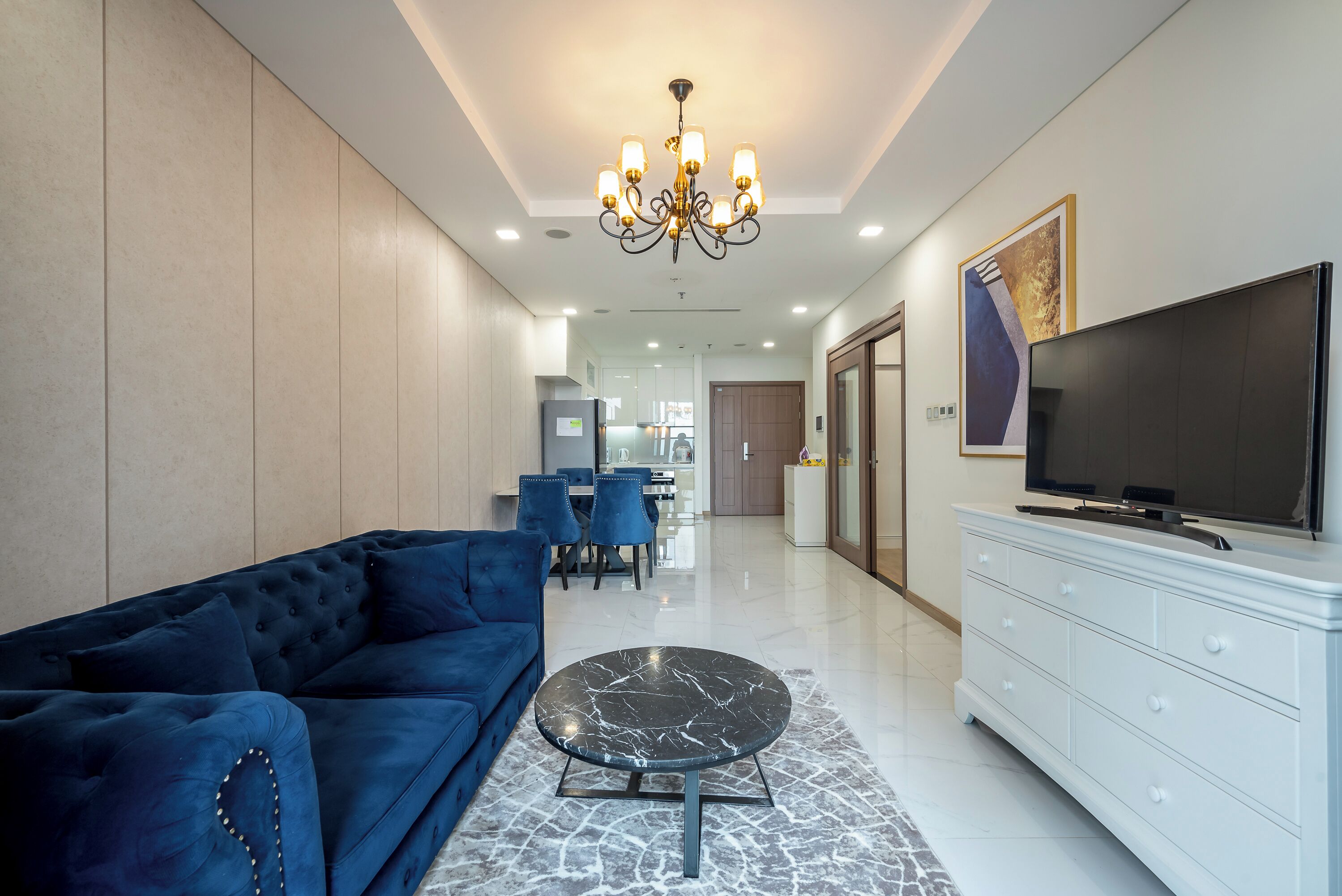 A modern living room with a blue sofa, a marble coffee table, and a TV on a white cabinet.