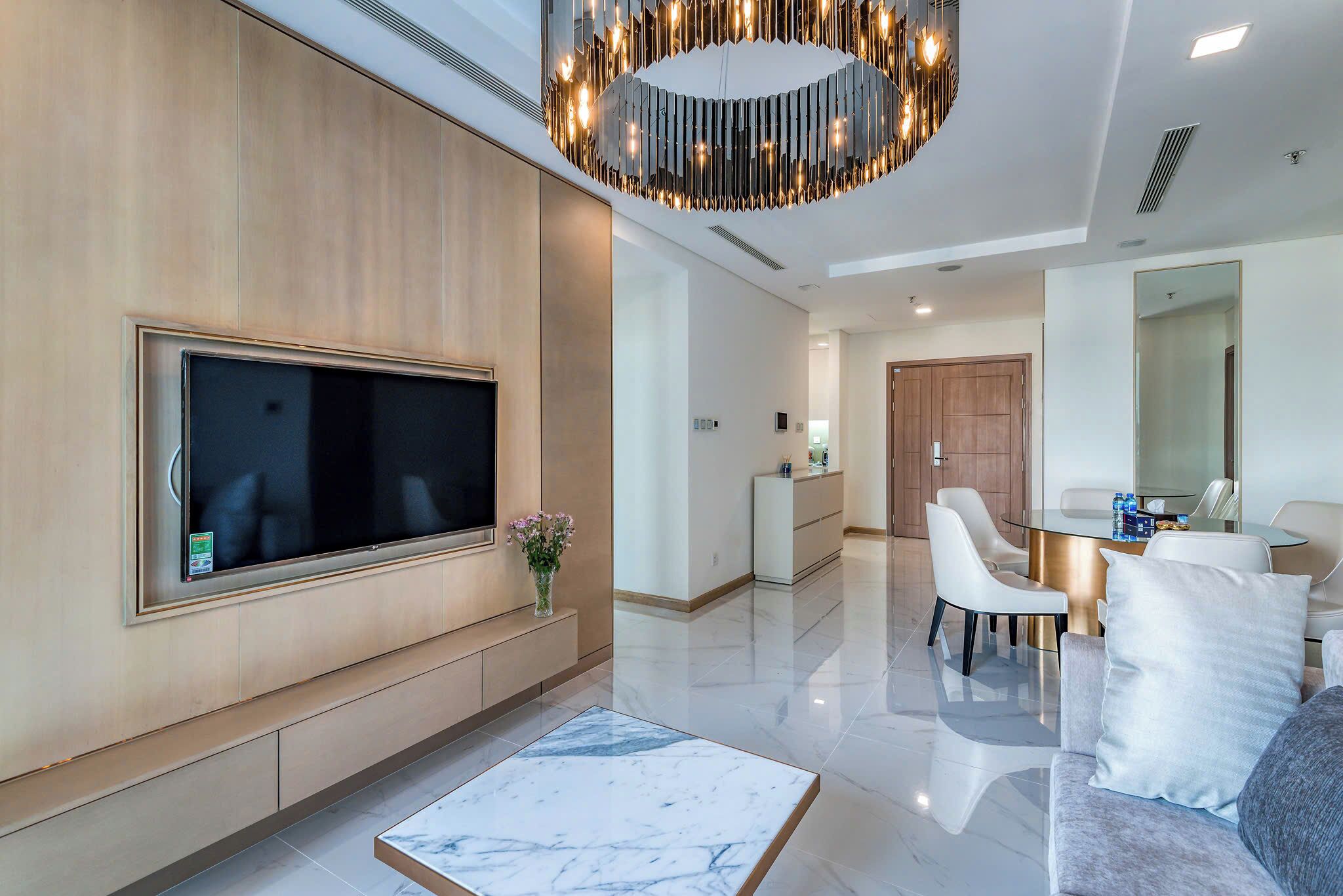 A modern living room with a flat-screen TV, a marble coffee table, and a dining area with a round table and chairs.