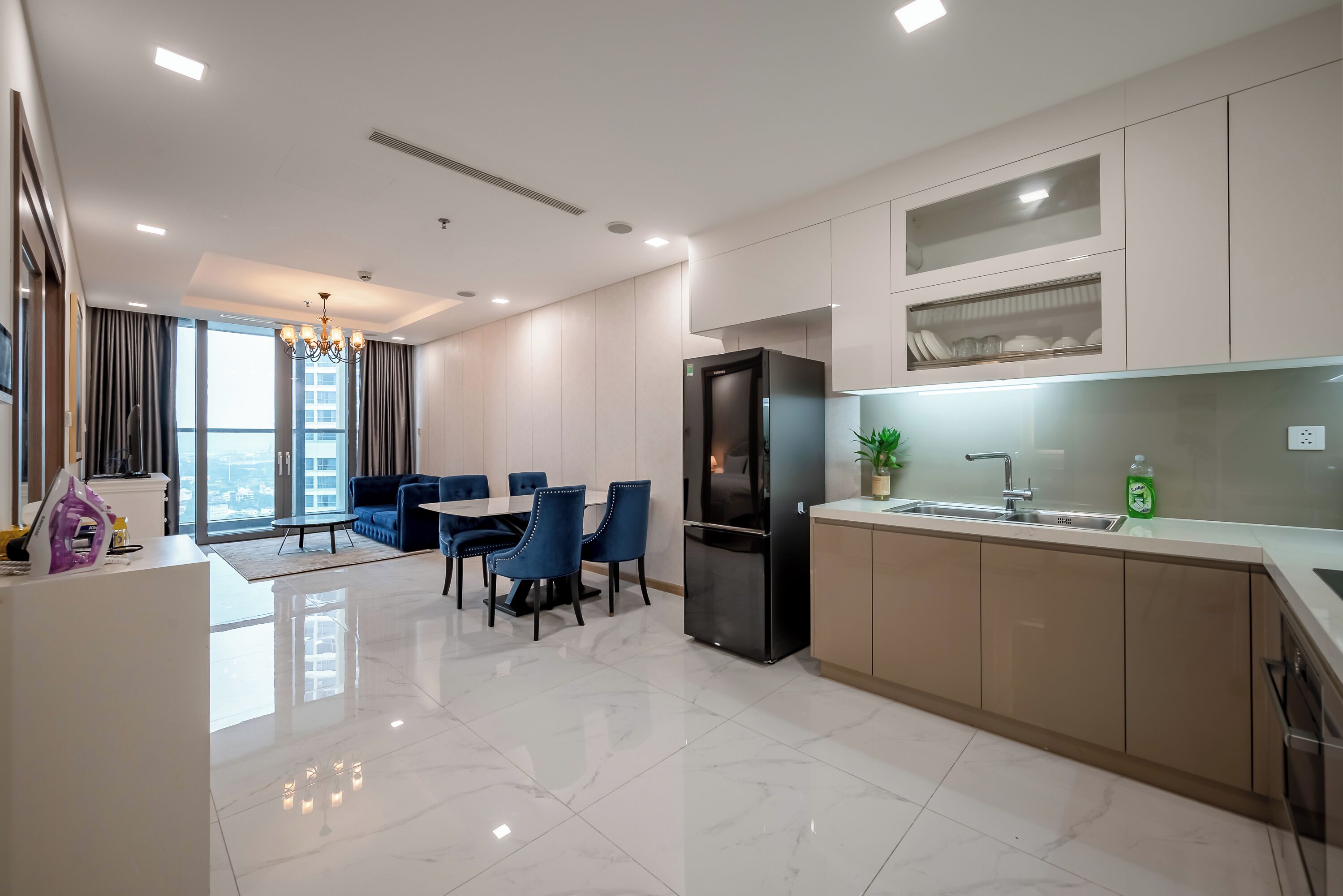 A modern kitchen with a black refrigerator, a dining area with blue chairs, and a large window with curtains.