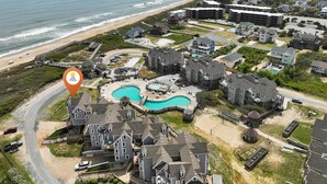 Vista aérea de una zona residencial costera con una gran piscina, propiedades frente a la playa y un muelle.