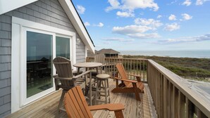 Una terraza de madera con muebles de exterior, una puerta de cristal y vistas al océano.