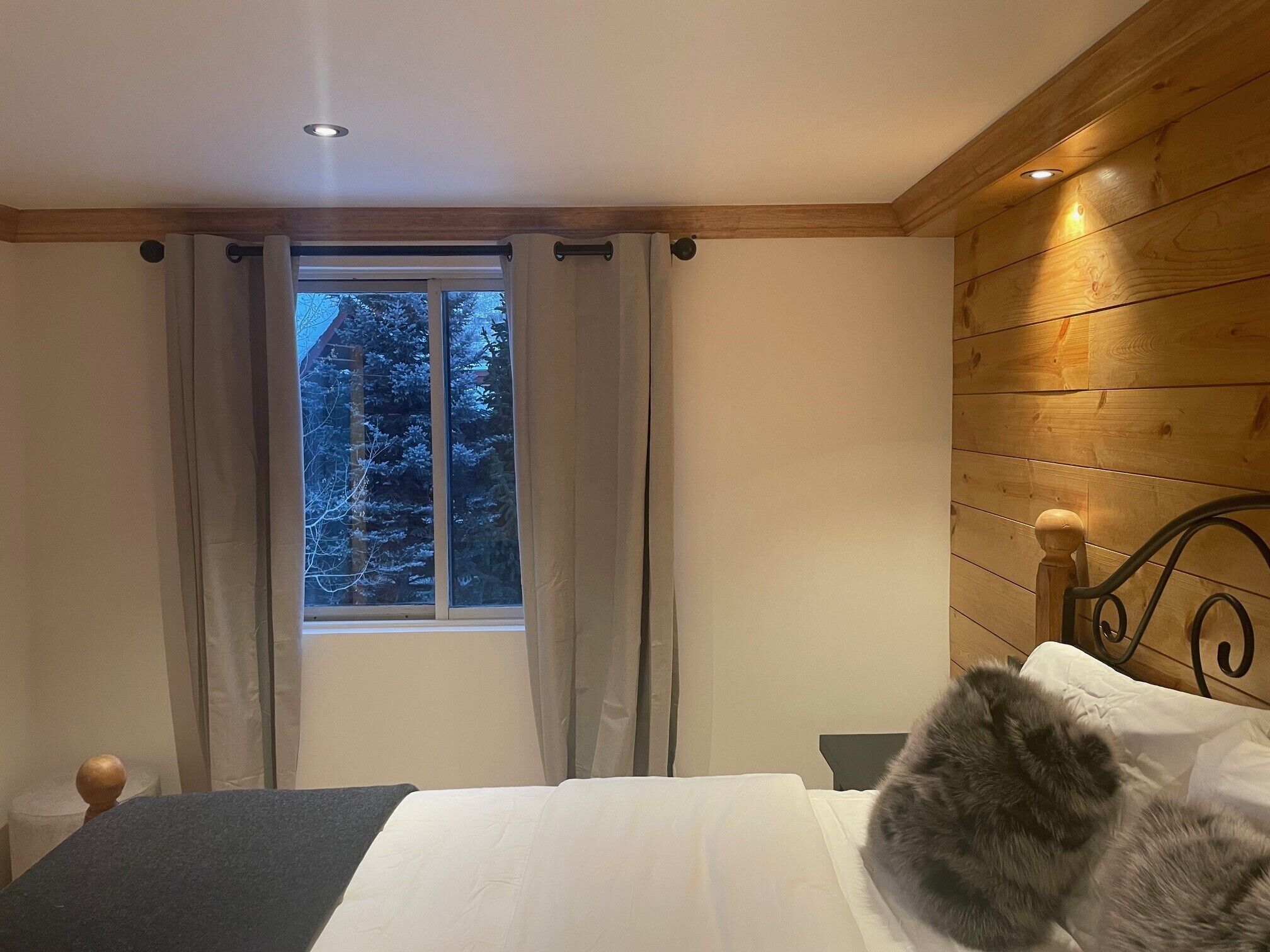 Une chambre à coucher avec un lit, des murs en bois, une fenêtre avec des rideaux et une vue sur les arbres à l’extérieur.