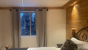 Ein Schlafzimmer mit einem Bett, Holzwänden, einem Fenster mit Vorhängen und Blick auf Bäume.