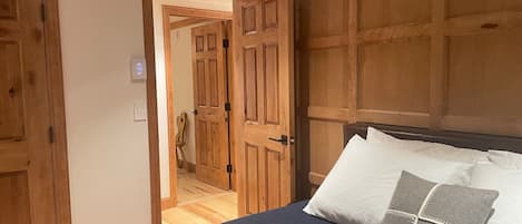 A bedroom with a bed, wooden wardrobe, and a door leading to another room.