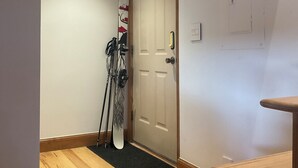 Ein Korridor mit Holzboden, einer Tür mit kleinem Fenster und einem Kleiderständer mit Ski.