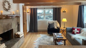 Ein gemütliches Wohnzimmer mit Kamin, einer Couch, einem Couchtisch und Blick auf eine verschneite Landschaft durch das Fenster.