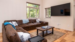 Una sala de estar con un sofá de cuero color café, una mesa de centro de madera y un televisor de pantalla plana montado en la pared.