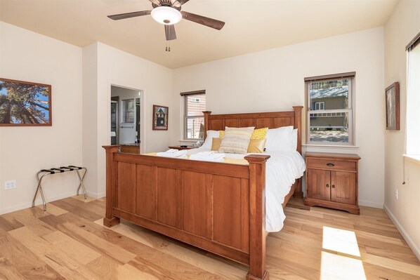 Une chambre à coucher avec un lit en bois, une table de chevet, un ventilateur de plafond et une fenêtre.