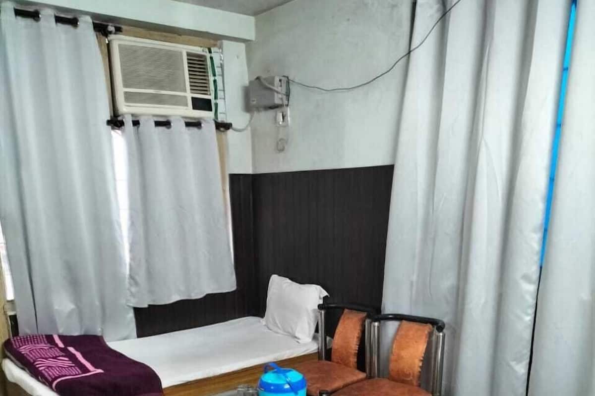A hotel room with a bed, a small table, a chair, a sofa, and an air conditioning unit.