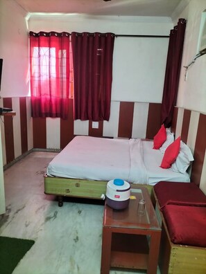 A bedroom with a bed, a bedside table, a heater, and a window with curtains. - Hotel City Heart (Haridwar)