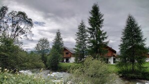 A house with a wooden deck and a river in the foreground. - Alpinest - Chalet Speiereck 1 (Mariapfarr)